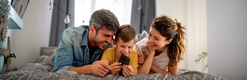 famiglia felice sul letto che guarda lo smartphone dopo aver attivato luce, gas e mobile con Enel