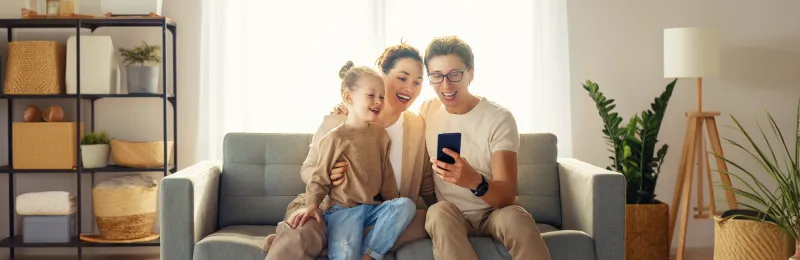 famiglia sorridente sul divano con lo smartphone dopo aver attivato gas e mobile con Enel